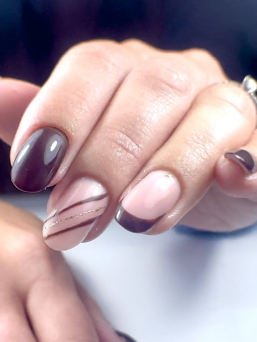 Short rounded nails in glossy plum-brown and nude, with a fine brown and gold stripe accent nail