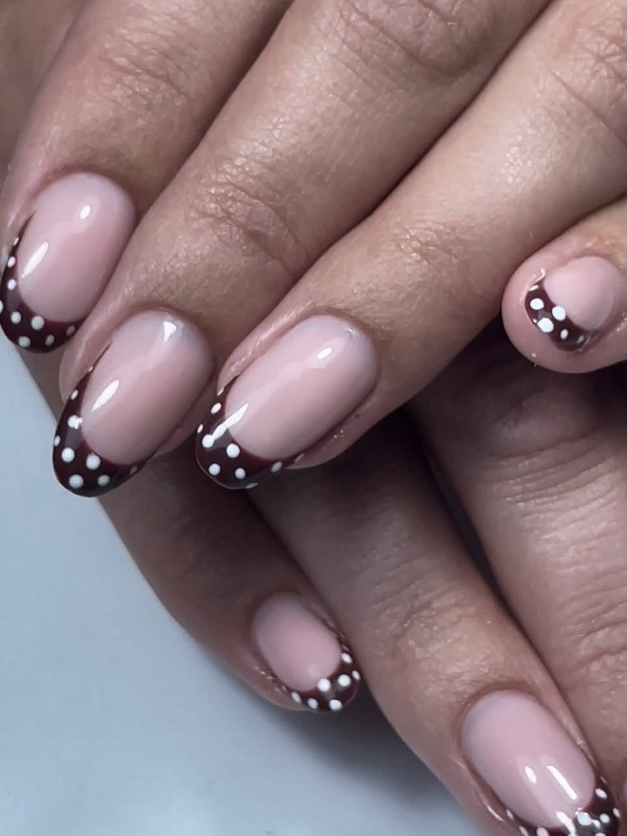 Nude almond nails with chocolate-brown French tips and tiny white polka dots