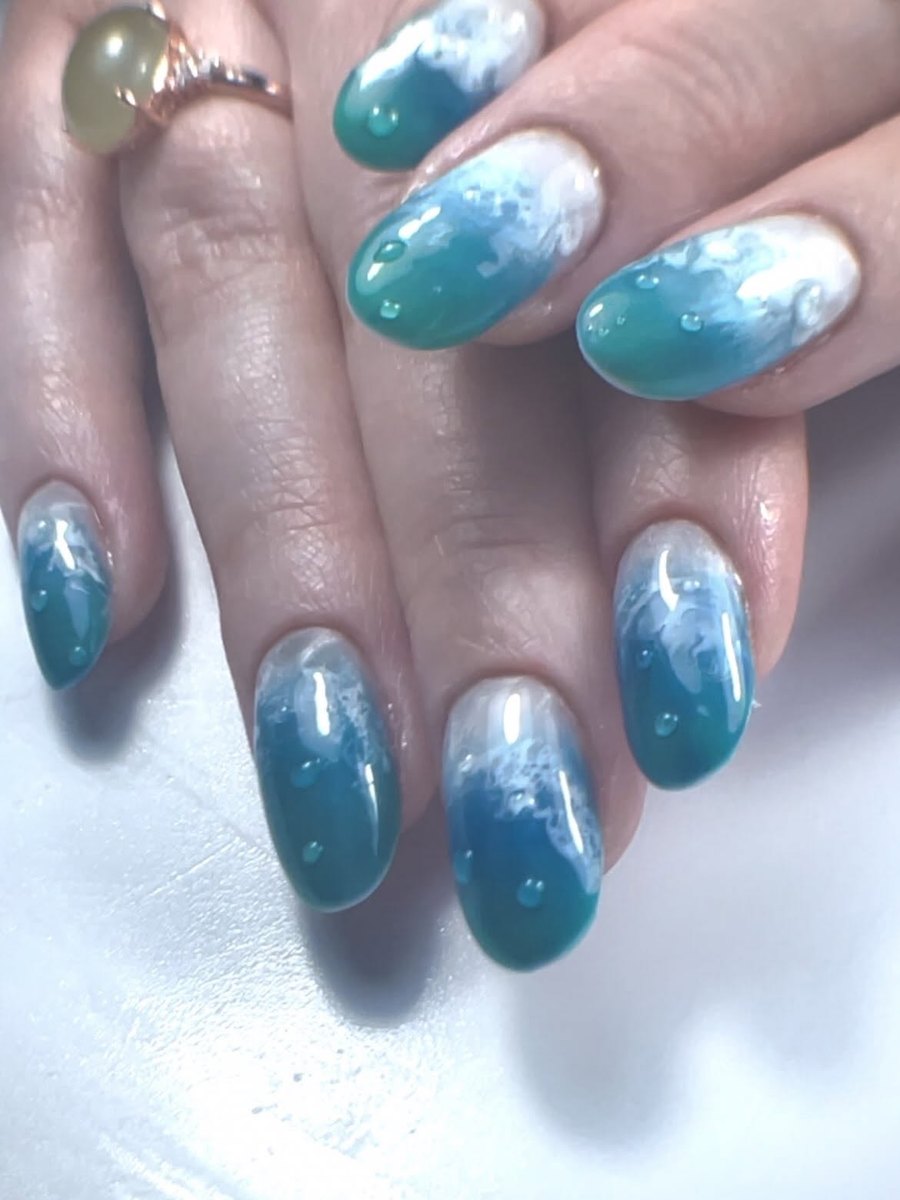 Teal and white ocean-wave nail art with water droplets on oval nails